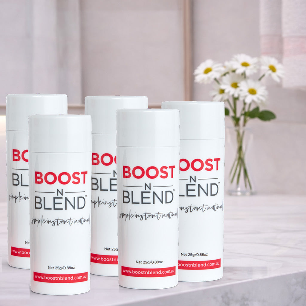 Five bottles of Boost N Blend hair fibres on a surface with a blurred background