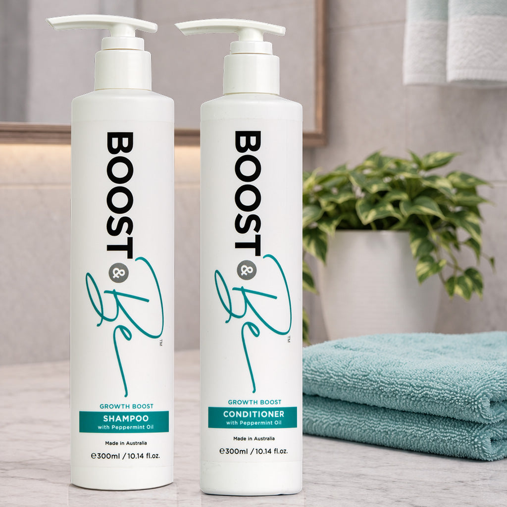 Boost & Be Growth Boost shampoo and conditioner on a bathroom counter with towels and a plant in the background.