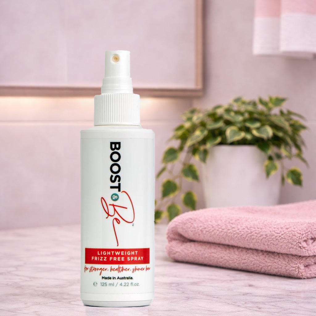 Boost & Be Lightweight Frizz Free hair spray bottle on a bathroom counter with towels and a plant in the background