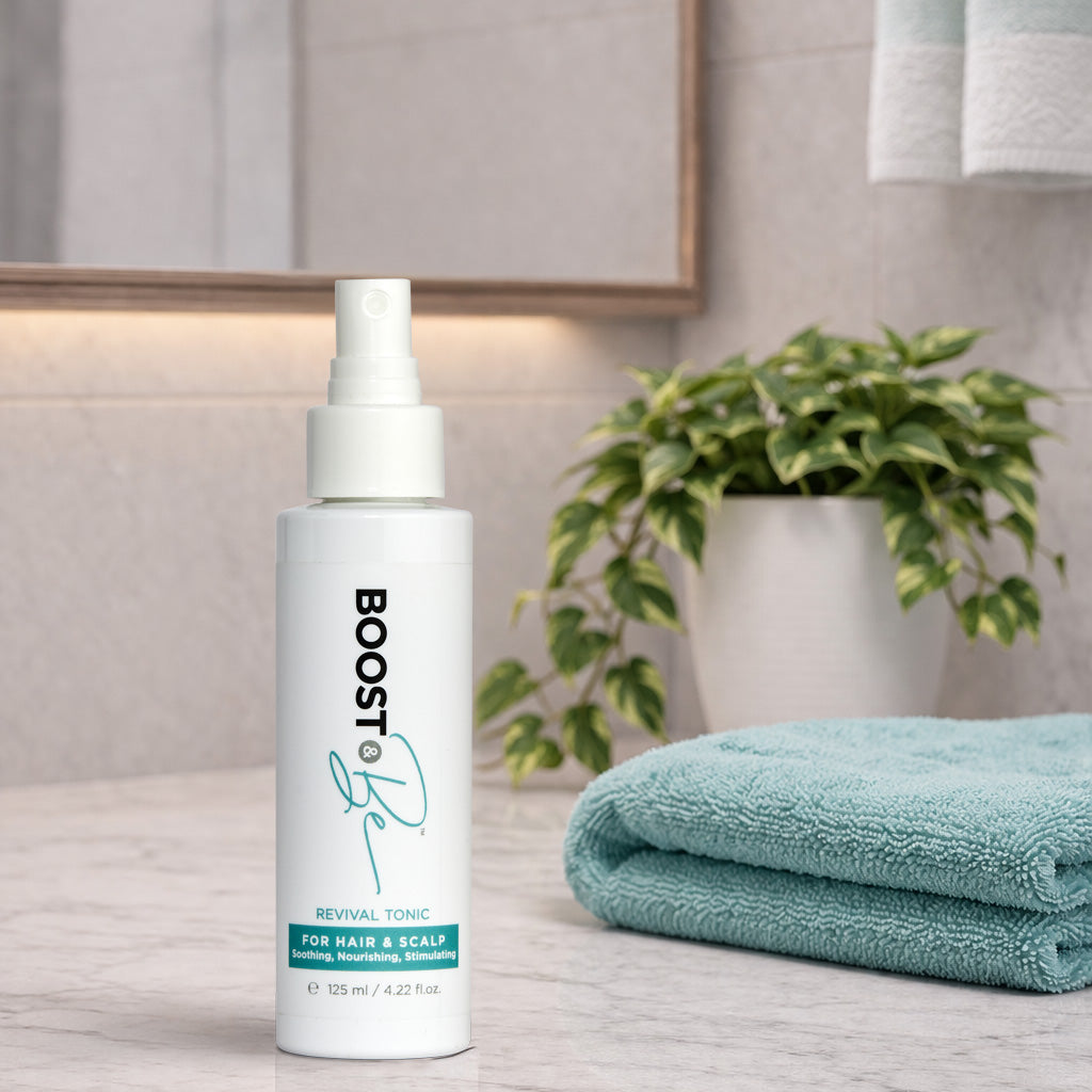 White bottle labeled BOOST & Be Revival Tonic for Hair & Scalp, on a wooden surface with a plant and towel in the background