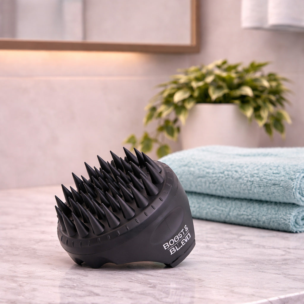 Black scalp massager on a bathroom counter with towels and a plant in the background