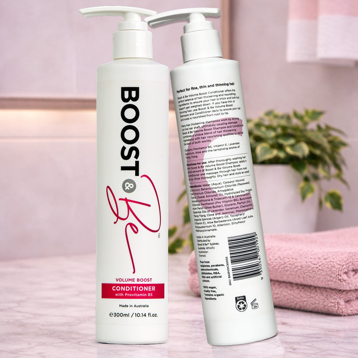 Boost & Be volume boost conditioner on a pink surface with a plant and towel in the background.