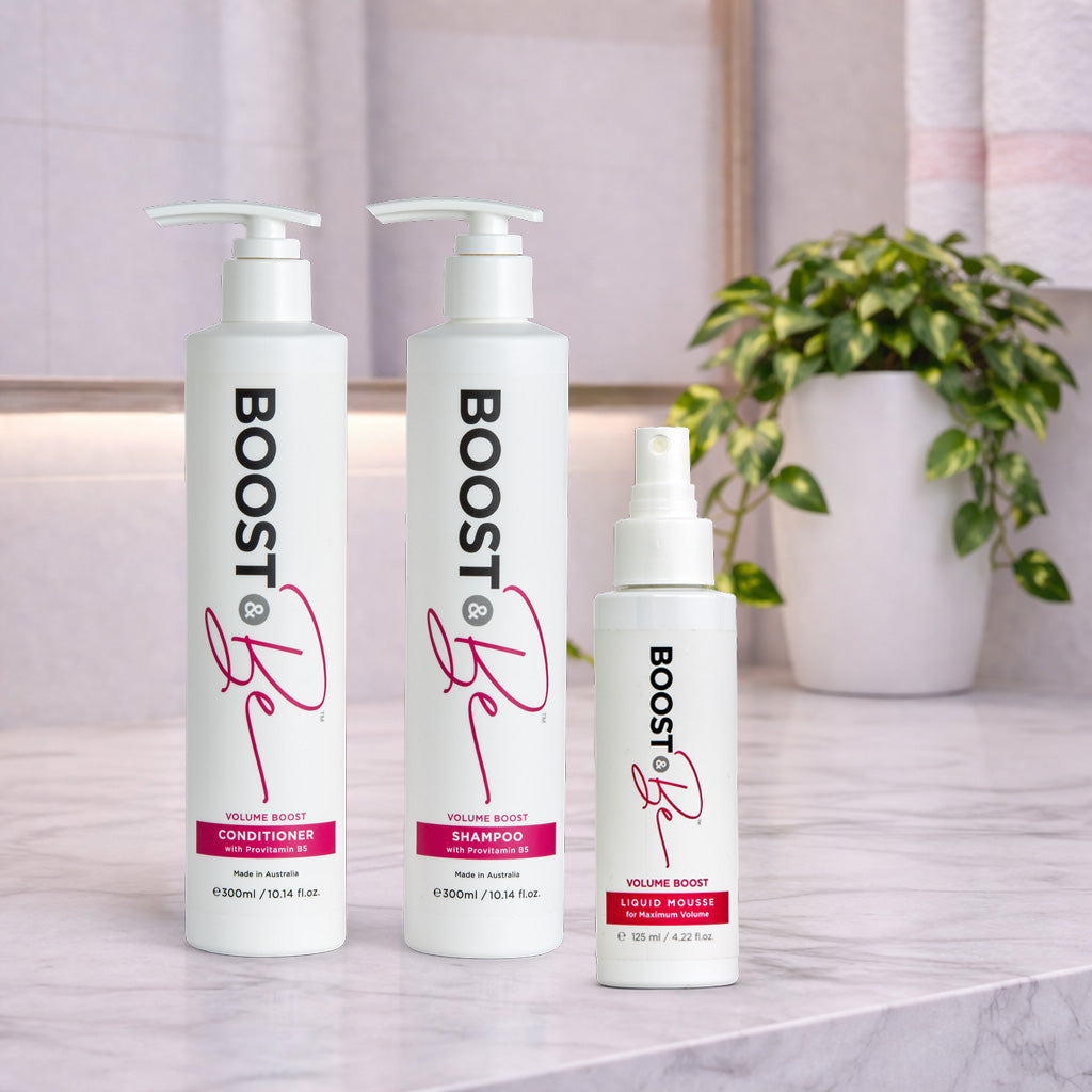 Boost & Be Volume Boost shampoo, conditioner and liquid mousse hair care products on a marble surface with a plant in the background.